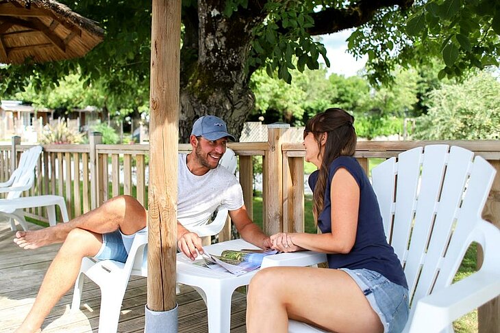 Relaxing terrace moment for an early booking couple Smiling couple sitting on a shaded campsite terrace, relaxing moment illustrating early booking couple.