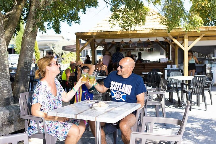 Couple enjoying a campsite bar terrace with early booking Couple toasting on a shaded campsite bar terrace, friendly moment illustrating an early booking couple.