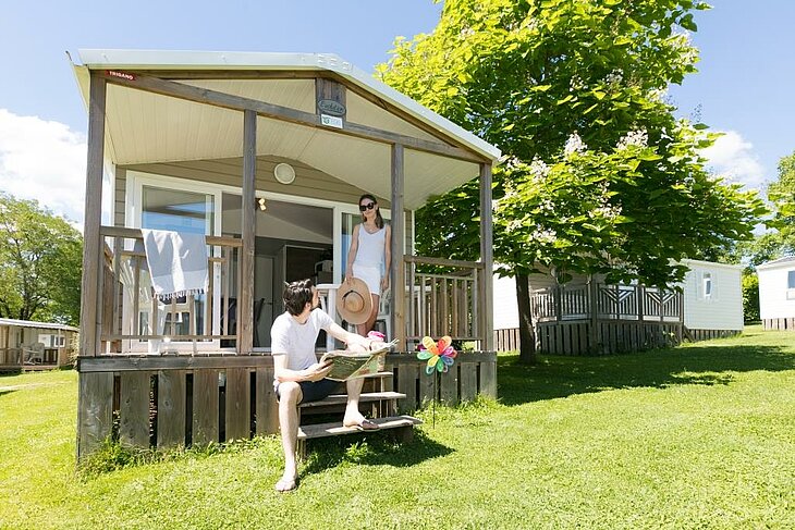 Couple by a nature mobile home with early booking couple Couple outside a bright mobile home in a human-scale nature campsite, illustrating the early booking couple experience.