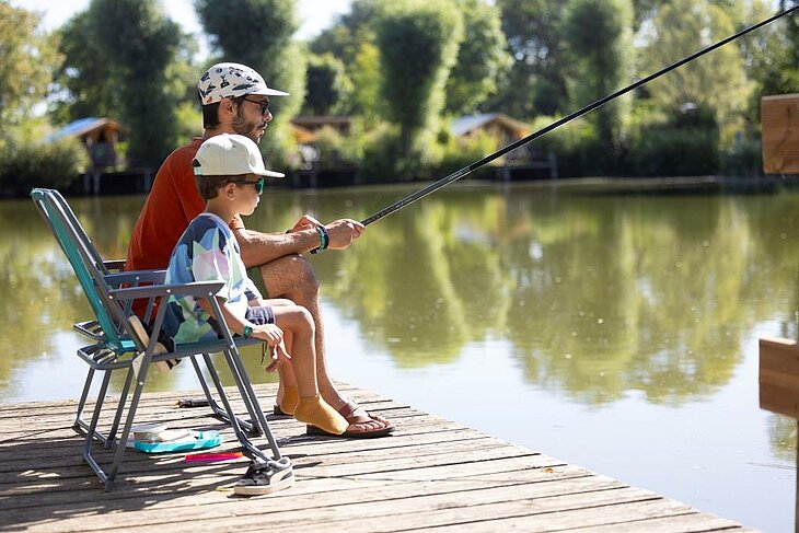 Father and child fishing by the lake at a nature campsite Father and child fishing by a campsite lake, peaceful nature moment supporting well-being and outdoor family time.
