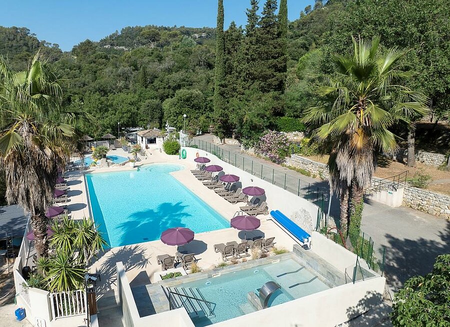 Swimming pool surrounded by sun loungers and palm trees at a Côte d’Azur campsite — the perfect setting for a family holiday.