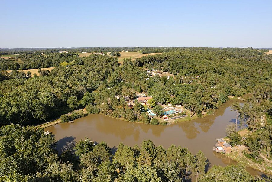 Aerial view of a campsite in Nouvelle-Aquitaine, surrounded by forest and bordered by a lake, perfect for a nature-filled holiday.