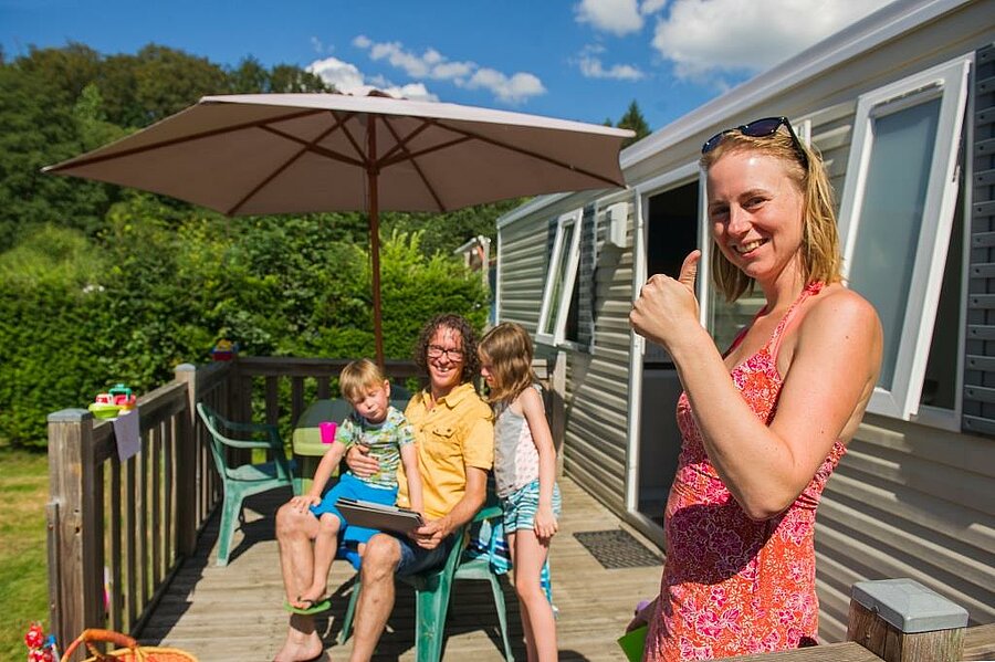 Smiling family in front of a mobile home, enjoying a budget-friendly campsite thanks to a great family holiday deal.